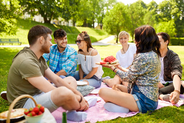 friendship, leisure and summer concept - group of happy friends eating watermelon at picnic in park