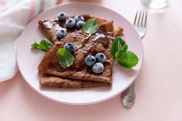 Homemade chocolate crepes served with blueberries, sauce and mint leaves on pink background. Selective focus. Top view. Copy space