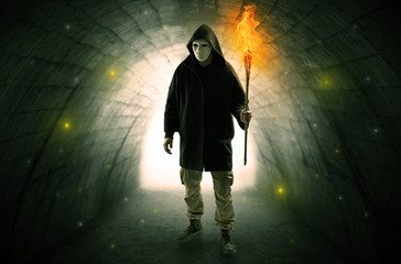 Ugly man with burning flambeau walking in a dark tunnel