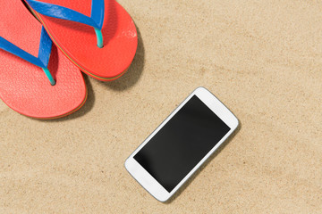 technology, vacation and summer holidays concept - smartphone and flip flops on beach sand
