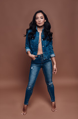 Fototapeta premium Denim style. Full length of beautiful young woman smiling and looking at camera while standing against brown background