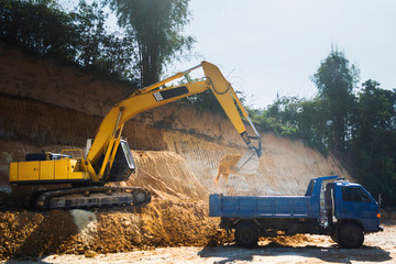 Industrial excavator and truck working on construction site to clear the land of sand and soil