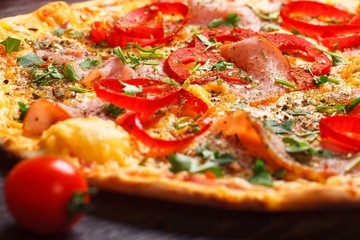 Close up Italian pizza with ham, cheese, pepper and herbs on a brown table decorated by mushrooms, red sweet pepper and cherry tomatoes