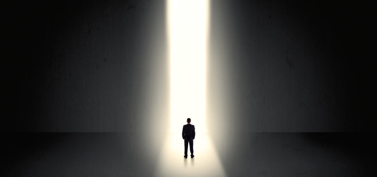 Businessman standing and seeing the light at the end of a big wall
