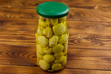 Delicious marinated mushrooms in glass jar on wooden table