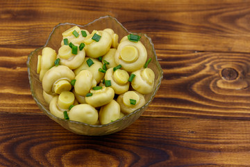 Glass bowl with pickled champignons. Marinated mushrooms on wooden table