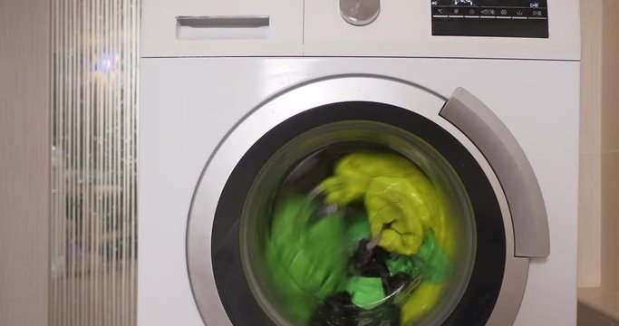 New washing machine of latest modification with rotating drum of vertical type. Bright baby clothes are loaded into washer.