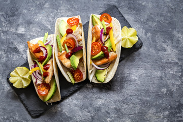 Mexican food tacos, fried chicken, greens,  avocado, pepper, red cabbage and avocado in tortillas on dark background