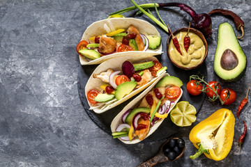 Mexican food tacos, fried chicken, greens,  avocado, pepper, red cabbage and avocado in tortillas on dark background