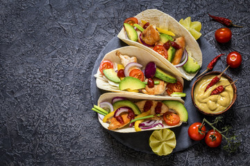 Mexican food tacos, fried chicken, greens,  avocado, pepper, red cabbage and avocado in tortillas on dark background
