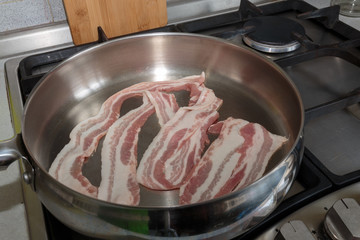 Raw strips of bacon, close-up, ready for cooking in a stainless frying pan.