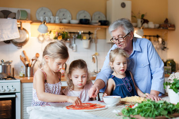 Pizza cooking class for kids, children chef. Cute girls are preparing italian food. Family dinner in cozy home kitchen. Three little sisters are helping old senior woman. Lifestyle moment.