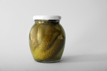 Glass jar with fermented cucumbers on light background
