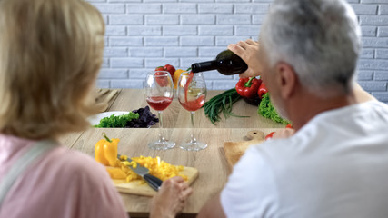 Romantic man pouring red wine in glasses, happy couple cooking together at home