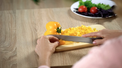 Female hands cutting fresh yellow pepper on chopping board in kitchen, cooking