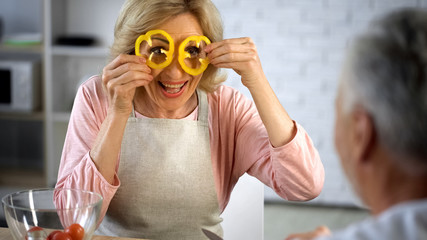 Positive wife in apron holding pepper slices front eyes, cooking hobby, health