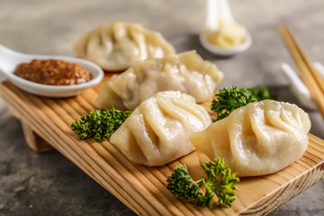 Wooden stand with tasty Japanese gyoza on grey background, closeup