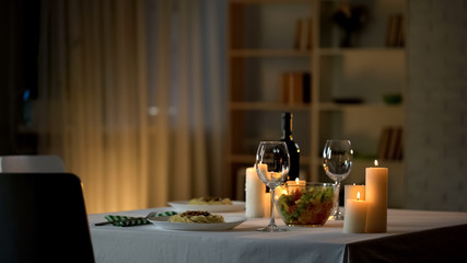 Romantic dinner table setting, wine glasses and fresh salad in bowl, home date