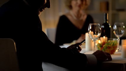 Elderly husband reading smartphone sms, ignoring wife on anniversary celebration