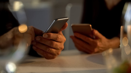 Adult couple scrolling smartphones instead romantic date in restaurant, ignore