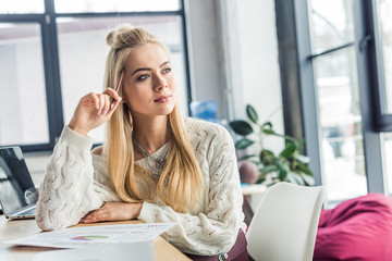 beautiful casual businesswoman sitting with document at desk in loft office and looking away