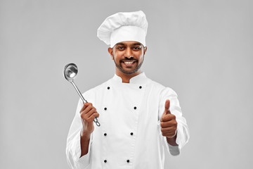 cooking, profession and people concept - happy male indian chef in toque with ladle showing thumbs...