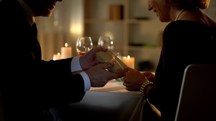 Loving aged man giving present to lady, retired couple celebrating anniversary