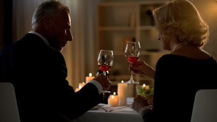 Elegant man and woman holding red wine glasses, senior couple on date, love