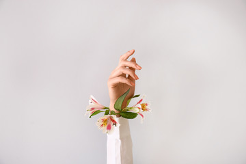 Female hand with beautiful flowers on light background