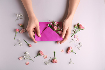 Fototapeta na wymiar Female hands with paper envelope and beautiful flowers on light background
