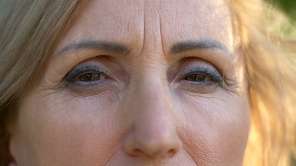 Mature wrinkled woman looking at camera, hope and despair in eyes, close up
