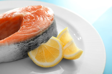 Raw salmon steak with lemon on plate, closeup