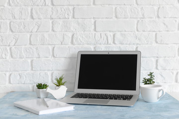 Comfortable workplace with modern laptop near white brick wall