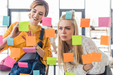 beautiful casual businesswomen looking at colorful sticky notes on glass window in office