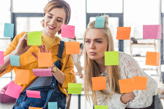 beautiful casual businesswomen looking at colorful sticky notes on glass window in office