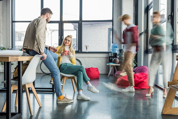 female and male casual businesspeople sitting and having discussion in loft office with colleagues in motion blur on background
