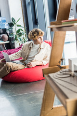 handsome casual businessman sitting in bean bag chair while using laptop in loft office