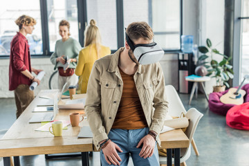 male designer in vr headset having virtual reality experience in loft office with colleagues on background