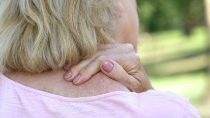 Mature woman massaging numb neck and shoulders, spine injury consequences