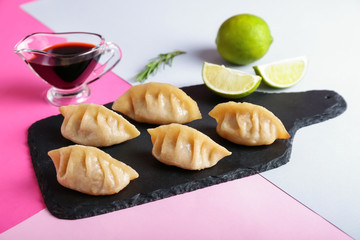 Slate plate with tasty Japanese gyoza and sauce on color background