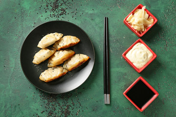 Plate with tasty Japanese gyoza and sauces on color background