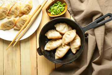 Frying pan and plate with tasty Japanese gyoza on wooden table