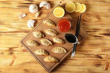 Board with tasty Japanese gyoza and sauces on wooden table