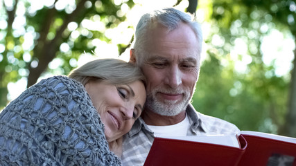 Loving mature family watching photoalbum, remembering childhood of their kids