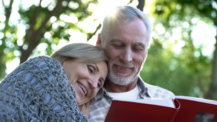 Fototapeta premium Happy old couple watching photobook and smiling, pleasant youth memories, fun