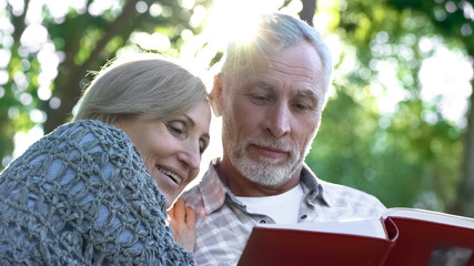 Naklejka premium Cute senior couple viewing photoalbum, remembering funny moments of life