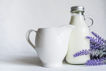 Vintage bottle with milk, next to a beautiful jug and a branch of lavender flowers on a white vintage background