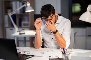 business, deadline and stress concept - tired businessman in eyeglasses working at night office