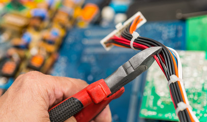 Connector, cables and hand with pliers. E-waste disposal close-up. Work of technical specialist. Colorful heap of old discarded laptop or PC parts in background. PCB, computer boards. Selective focus.