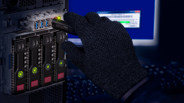 Hand in black glove holding USB flash drive. Computer data theft detail. Spy or saboteur is copying secret information from a server with dark hot-swap hard disks. Concept of cyber crime or espionage.